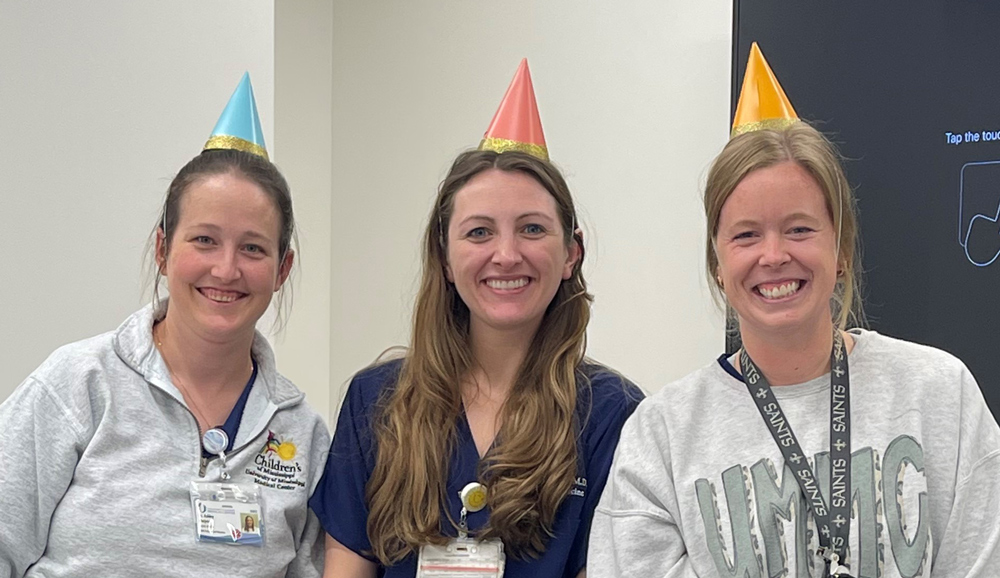 Three smiling medical students wearing birthday hats.